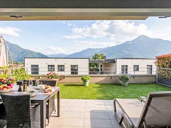 A patio with a dining table and chairs, a small lawn, and a view of mountains.