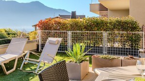A rooftop terrace with two lounge chairs, a dining table, and potted plants.