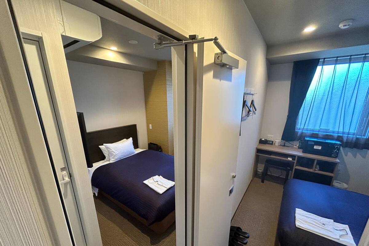 A hotel room with a bed, a desk, a chair, and a window with curtains.