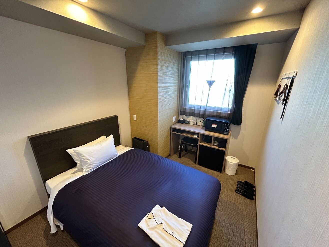 A hotel room with a bed, desk, chair, and a window with curtains.