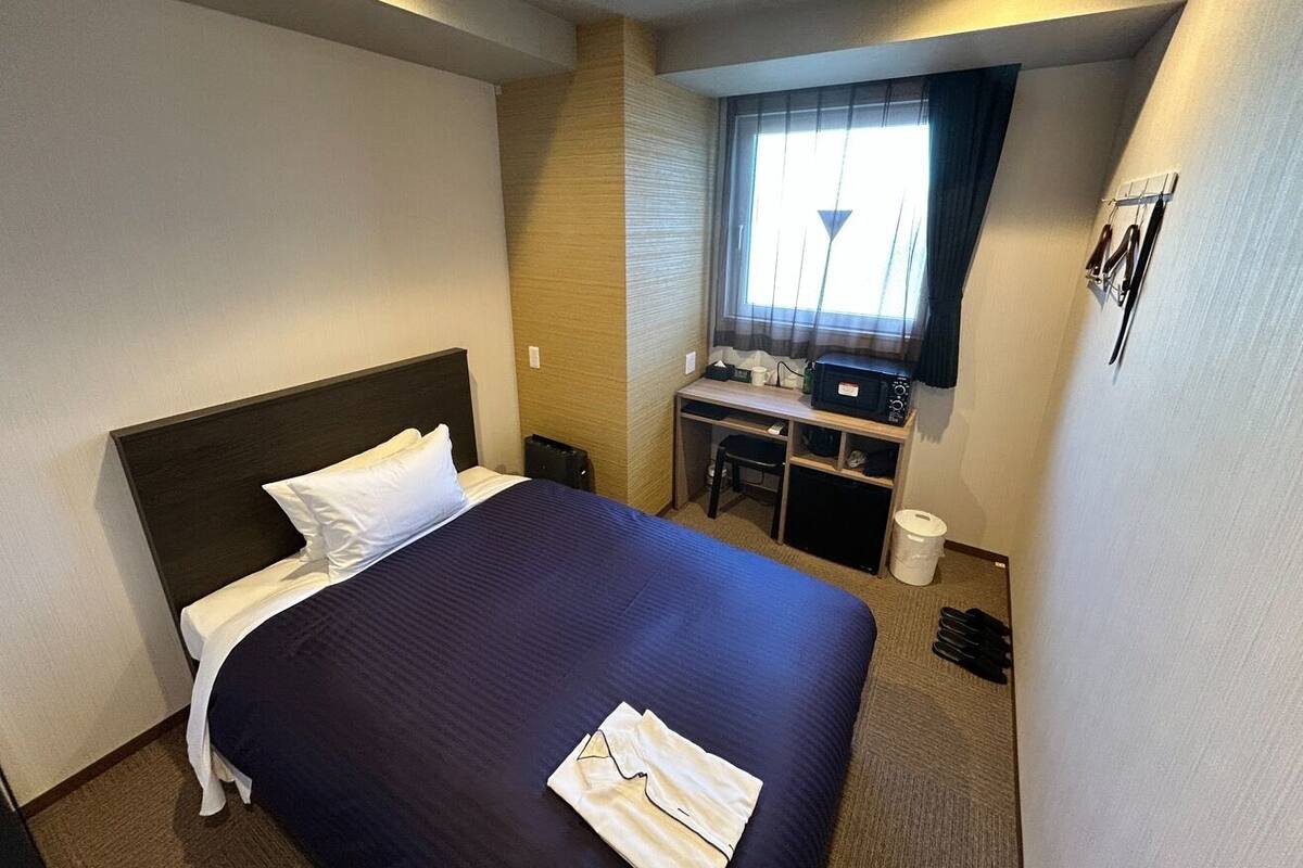 A hotel room with a bed, desk, chair, and a window with curtains.