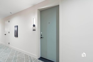 A hallway with a closed door, a wall-mounted light, and a door number sign.