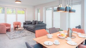 A modern living room with a grey sofa, pink armchairs, and a wooden dining table set for breakfast. - "Experience unforgettable days in the Dangaster Düne!" (Dangast)