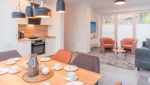 A modern kitchen with white cabinets, a dining area with a wooden table set for breakfast, and a living area with two chairs and a coffee table. - "Experience unforgettable days in the Dangaster Düne!" (Dangast)
