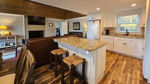 A kitchen with a wooden floor, white cabinets, a granite countertop, and a built-in island with stools. - 228 Lakeland (Anderson)