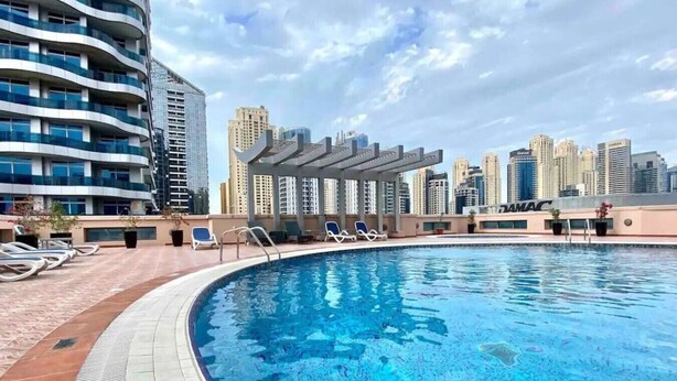 Una piscina en la azotea con sillones de descanso y una pérgola, rodeada de edificios altos.
