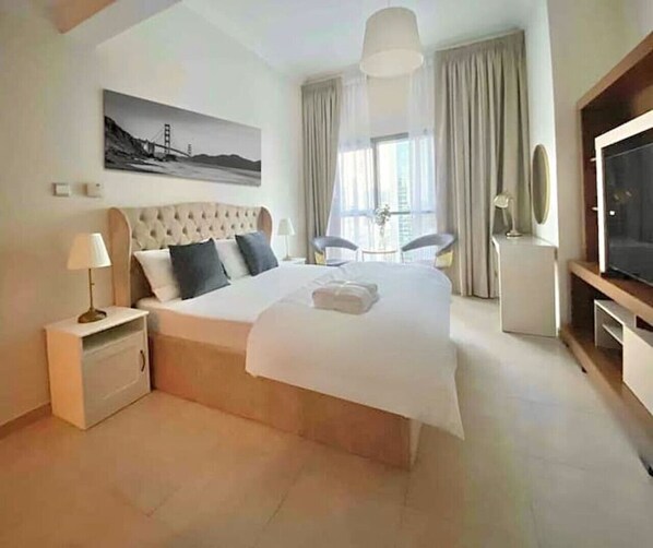 A hotel room with a large bed, a TV, a painting of a bridge, and a window with curtains.