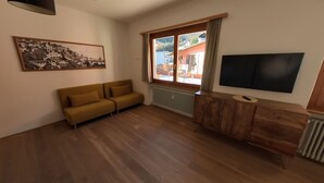 A living room with a sofa, a TV, a radiator, and a window with a view of the outside. - 7 Rooms (Losone)