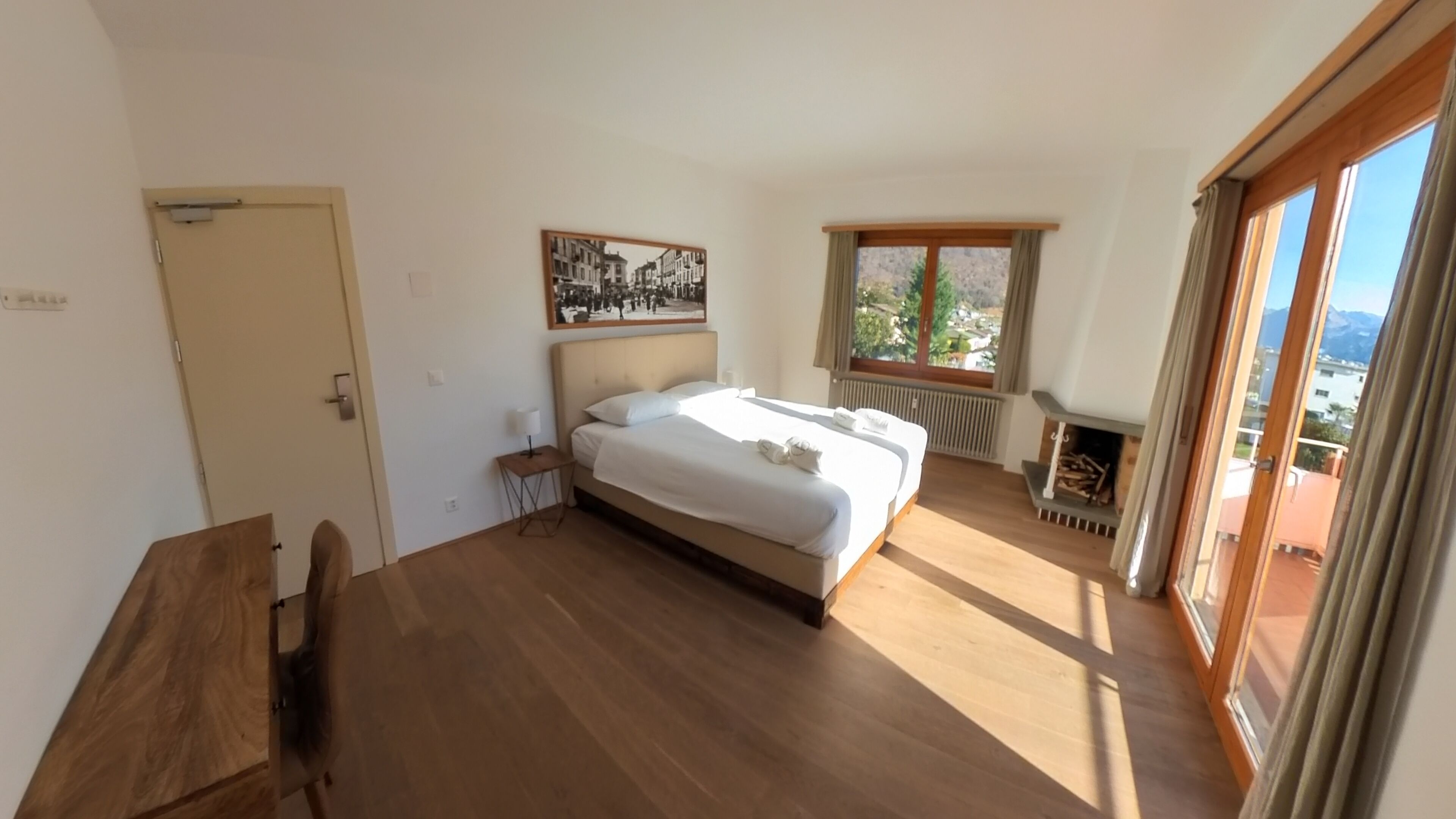 Un dormitorio con cama, una mesita, ventana con vistas y chimenea.
