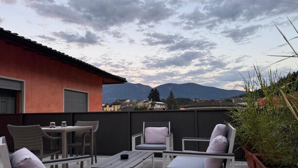 An outdoor patio with wicker furniture, a table, and a potted plant. - 7 Rooms (Losone)
