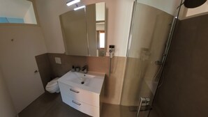 A modern bathroom with a white sink, a large mirror, and a glass shower enclosure. - 7 Rooms (Losone)