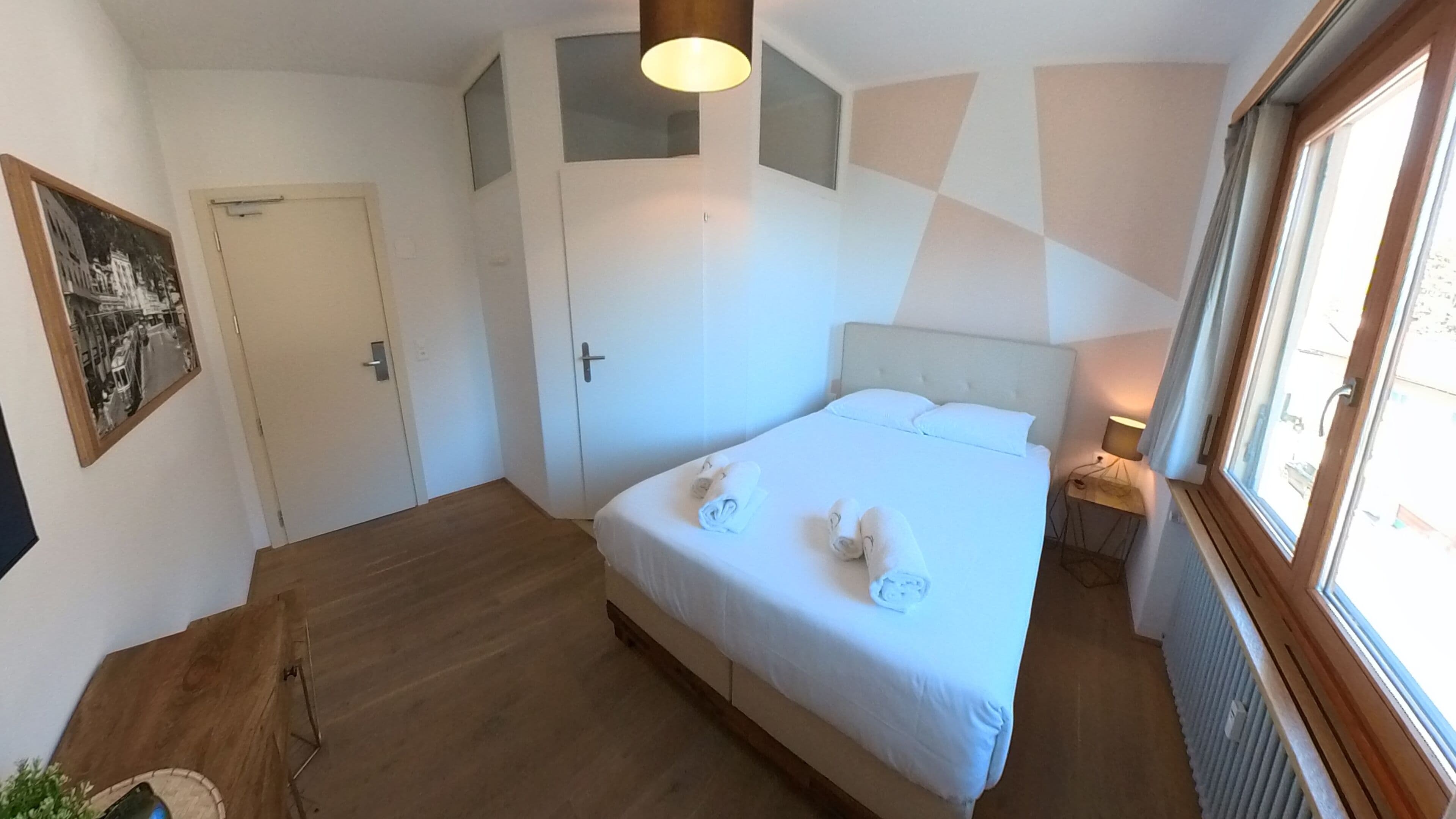 Een slaapkamer met een bed, nachtkastje, lamp, raam en deur.