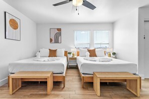 A modern hotel room with two beds, a ceiling fan, and a view of the city through large windows. - Pickleball Paradise: 6BR Home w/Pool+GameRoom Fun! (North Las Vegas)