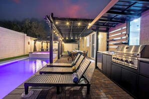 Un patio exterior con piscina, sillas de descanso y zona de barbacoa.