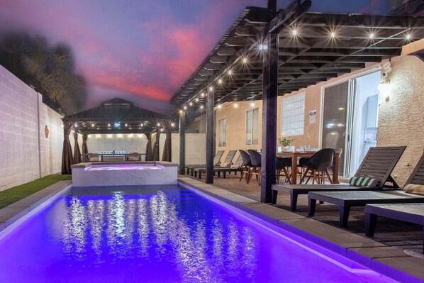 Una piscina con fuente, rodeada de sillones de descanso y un porche cubierto.