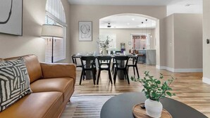 Un salon moderne avec un canapé en cuir marron, un coin repas doté d’une table ronde et une cuisine en arrière-plan.