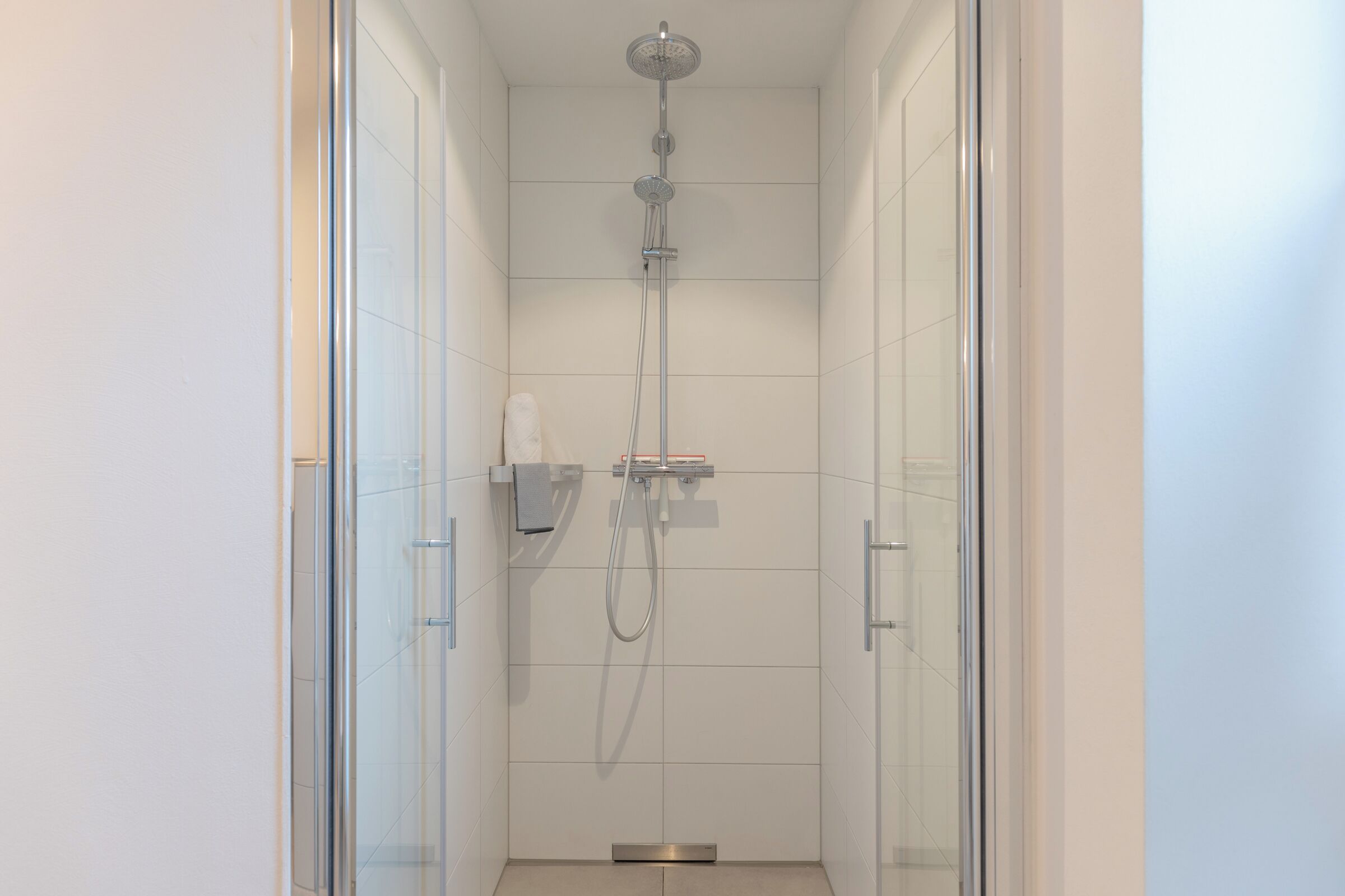 Una ducha moderna con cabezal de ducha manual y grifo empotrado, separada por puertas de vidrio.