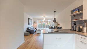 A modern kitchen with white cabinets, a central island, and a dining area with a sofa and coffee table. - Vacation apartment "Theos Garten" in Husum for up to 4 people (Husum)
