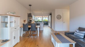 A modern apartment with a kitchen, dining area, and living room. It features wooden flooring, a sofa, a coffee table, and a view through the glass door. - Vacation apartment "Theos Garten" in Husum for up to 4 people (Husum)