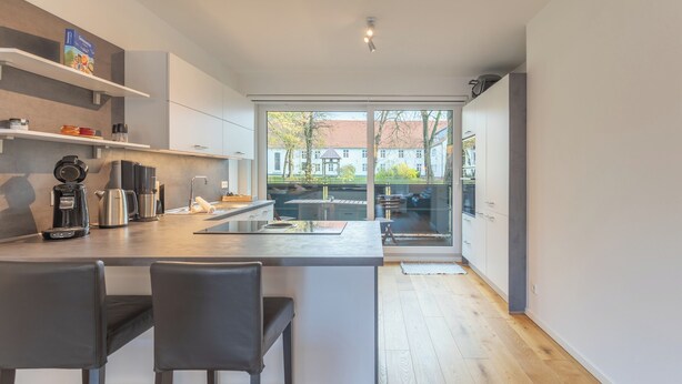 A modern kitchen with a central island, bar stools, and a view of the outside. - Vacation apartment "Theos Garten" in Husum for up to 4 people (Husum)