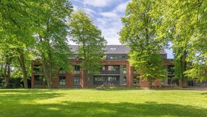 A modern building with a brick facade, large windows, and a surrounding grassy area with trees. - Vacation apartment "Theos Garten" in Husum for up to 4 people (Husum)