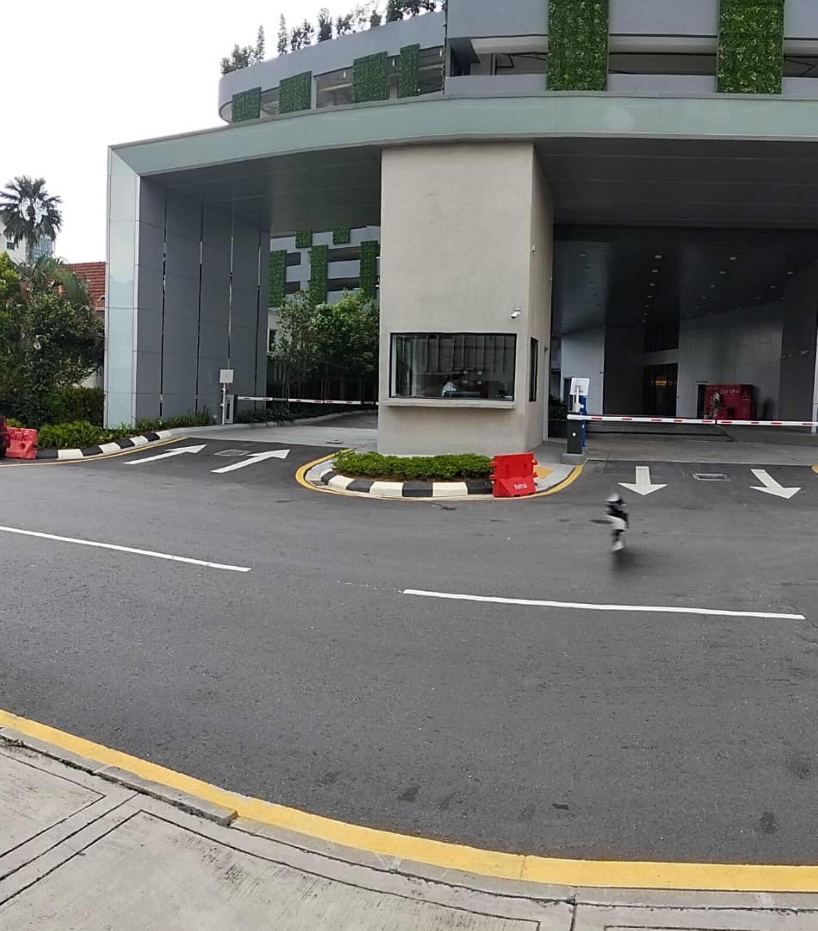 A modern building with a large entrance, a pedestrian crossing, and directional arrows on the road.