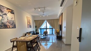 A modern dining area with a long table, chairs, and a sofa. There is a large window with curtains, a ceiling fan, and an air conditioning unit on the wall. - AGILE Infinity Suites TRX By AR (Kuala Lumpur)