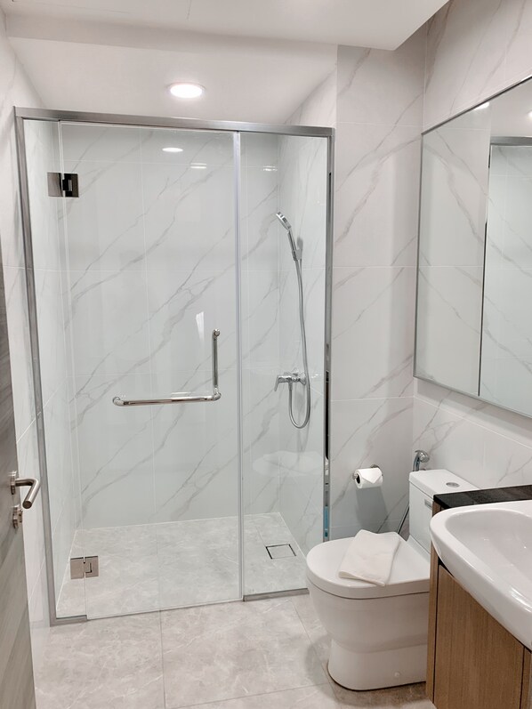 Une salle de bain moderne dotée d’une douche à parois de verre, de toilettes et d’un lavabo.