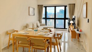A modern dining area with a large table set for four, a sofa, and a TV stand with a lamp. - AGILE Infinity Suites TRX By AR (Kuala Lumpur)