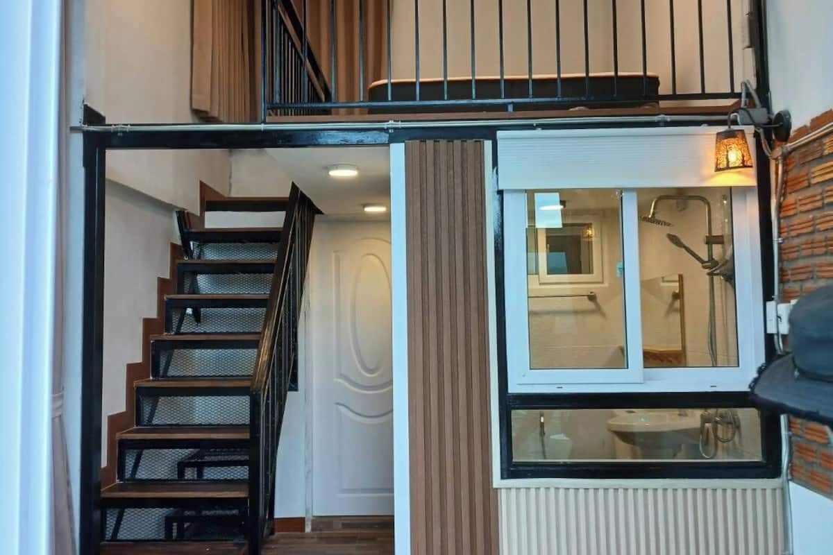 A modern interior with a staircase leading to a loft bedroom, a kitchen area with a window, and a radiator.