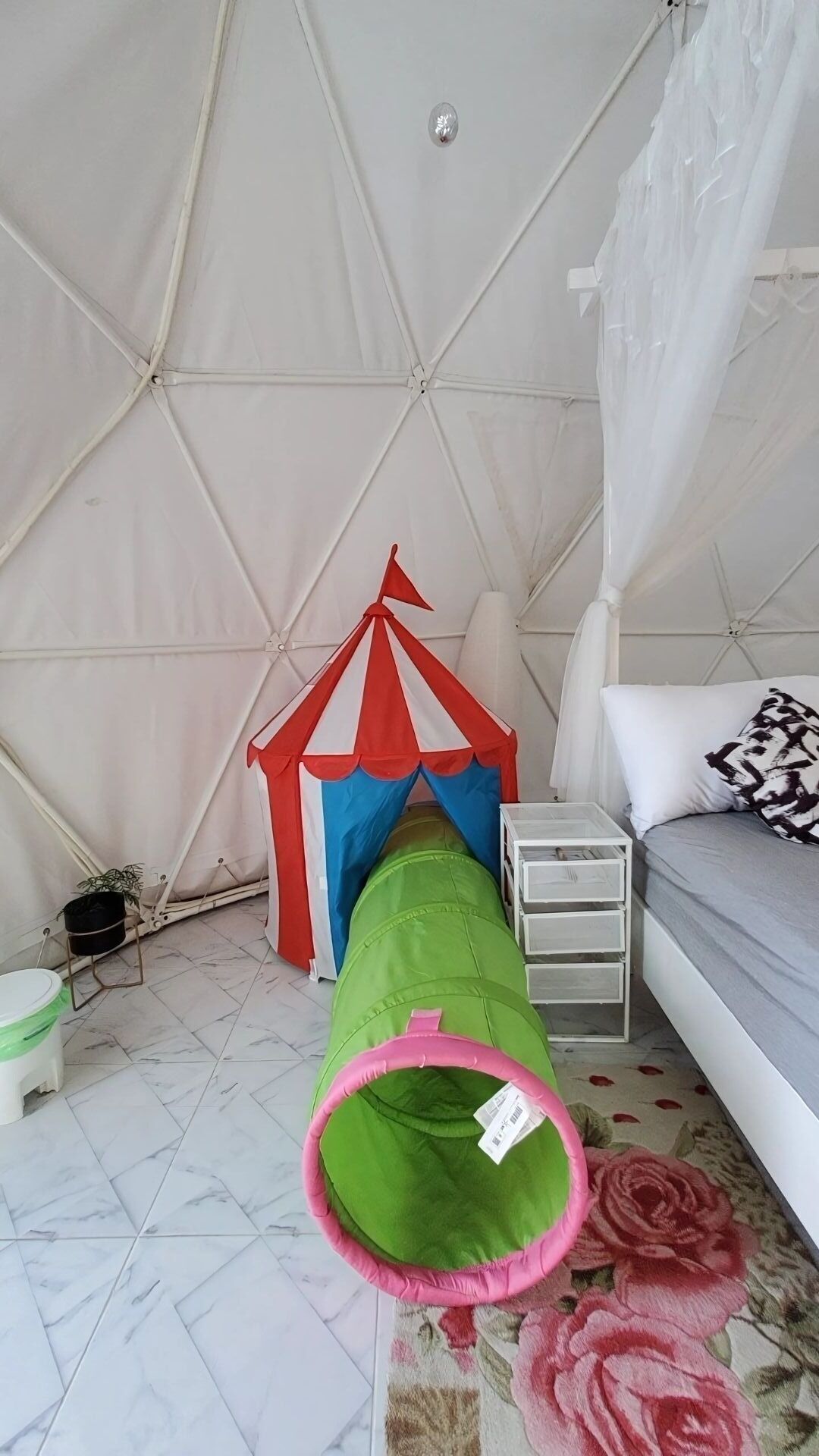 Una habitación con tienda de campaña, una cama, una mesita y un saco de dormir verde.