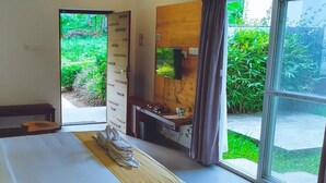A bedroom with a bed, a desk, a TV, and a view of greenery outside. - Thapovan  (Kodaikanal)