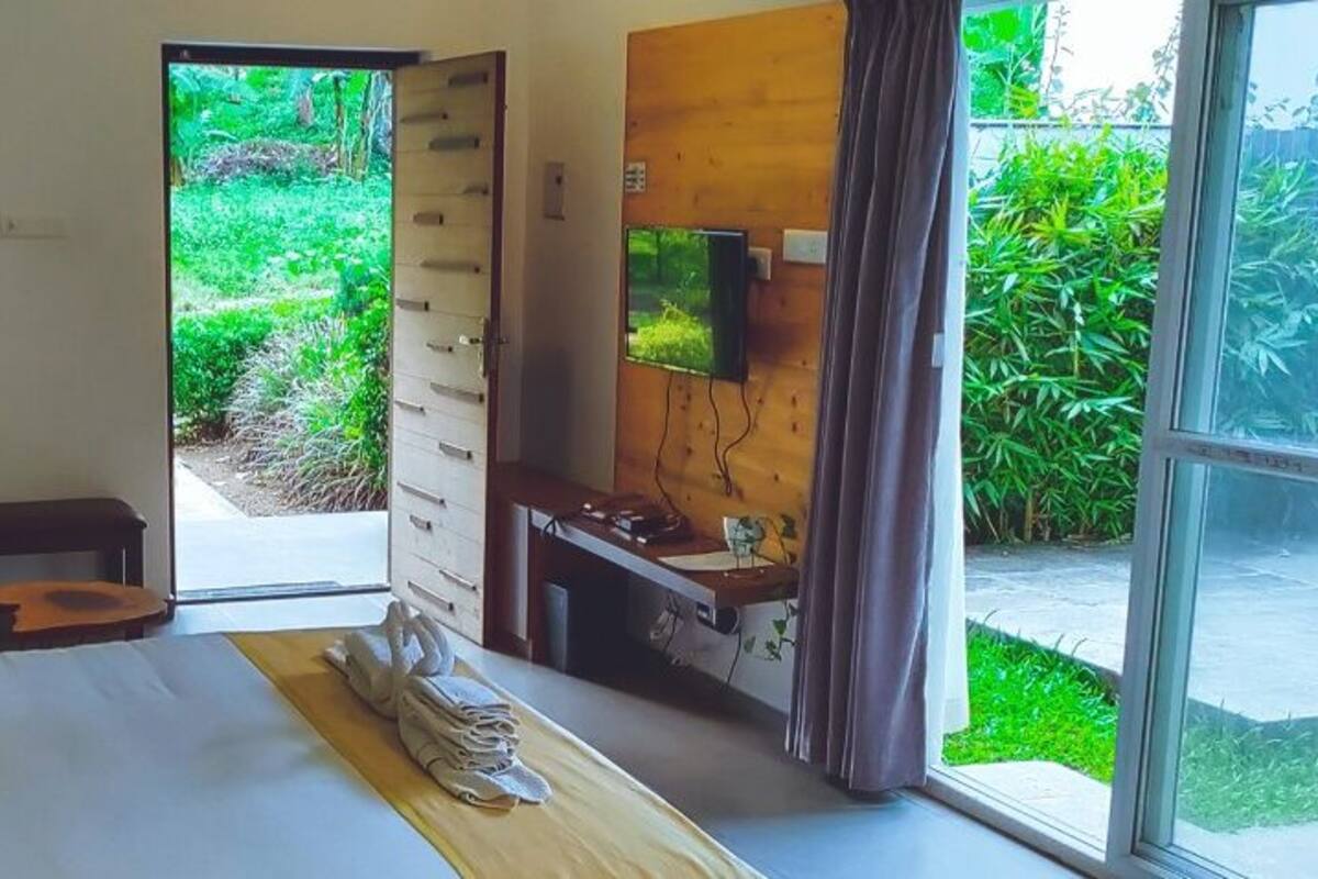 A bedroom with a bed, a desk, a TV, and a view of greenery outside.