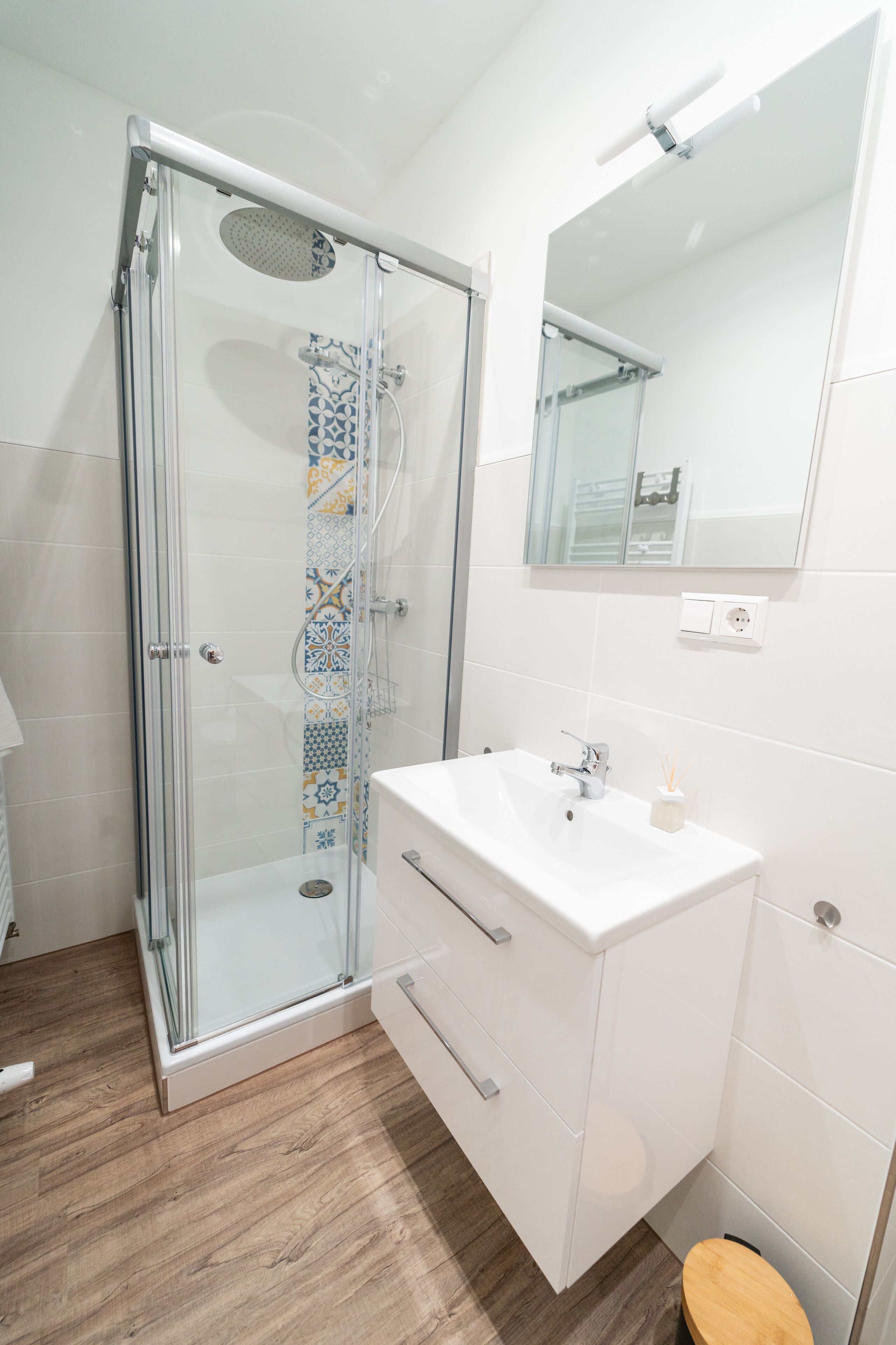 A modern bathroom with a glass-enclosed shower, a white sink with a mirror above, and a wooden toilet seat.