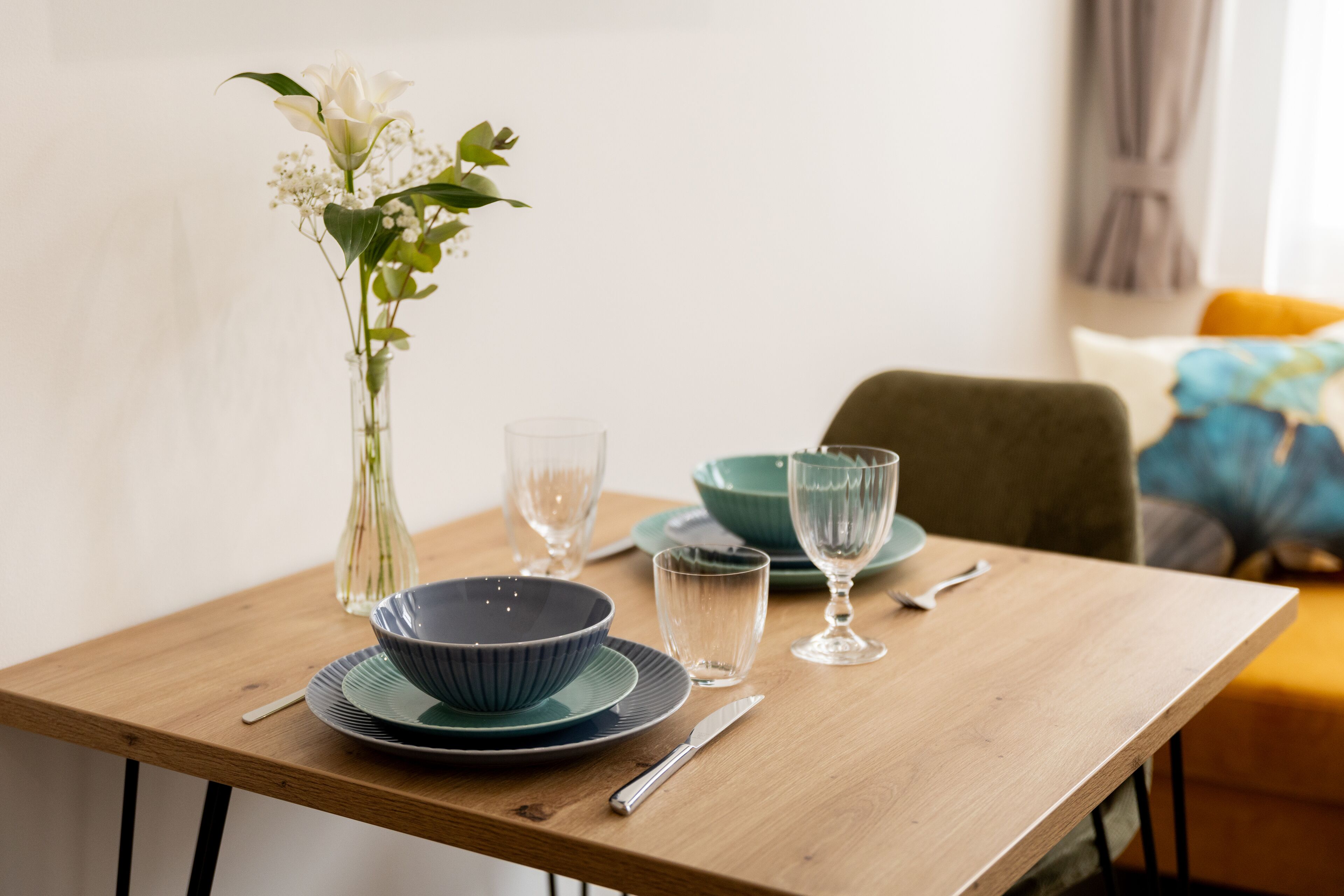 A dining table with a vase of flowers, plates, bowls, and cutlery.