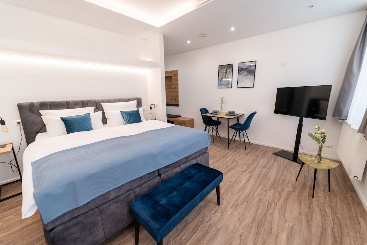 A modern hotel room with a large bed, a bench, a desk, and a TV.