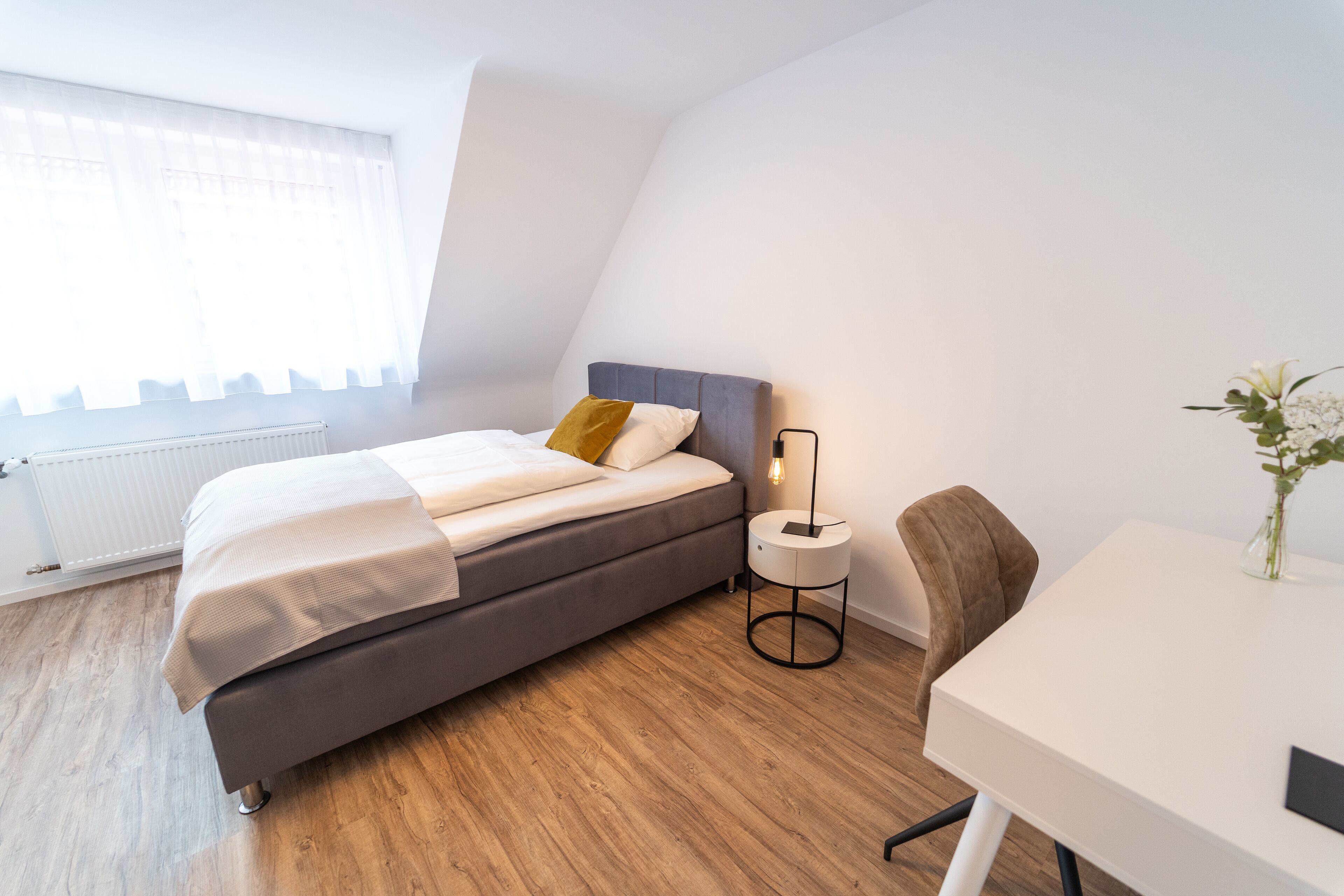 Un dormitorio moderno con cama, mesita de noche y una pequeña mesa con un florero.