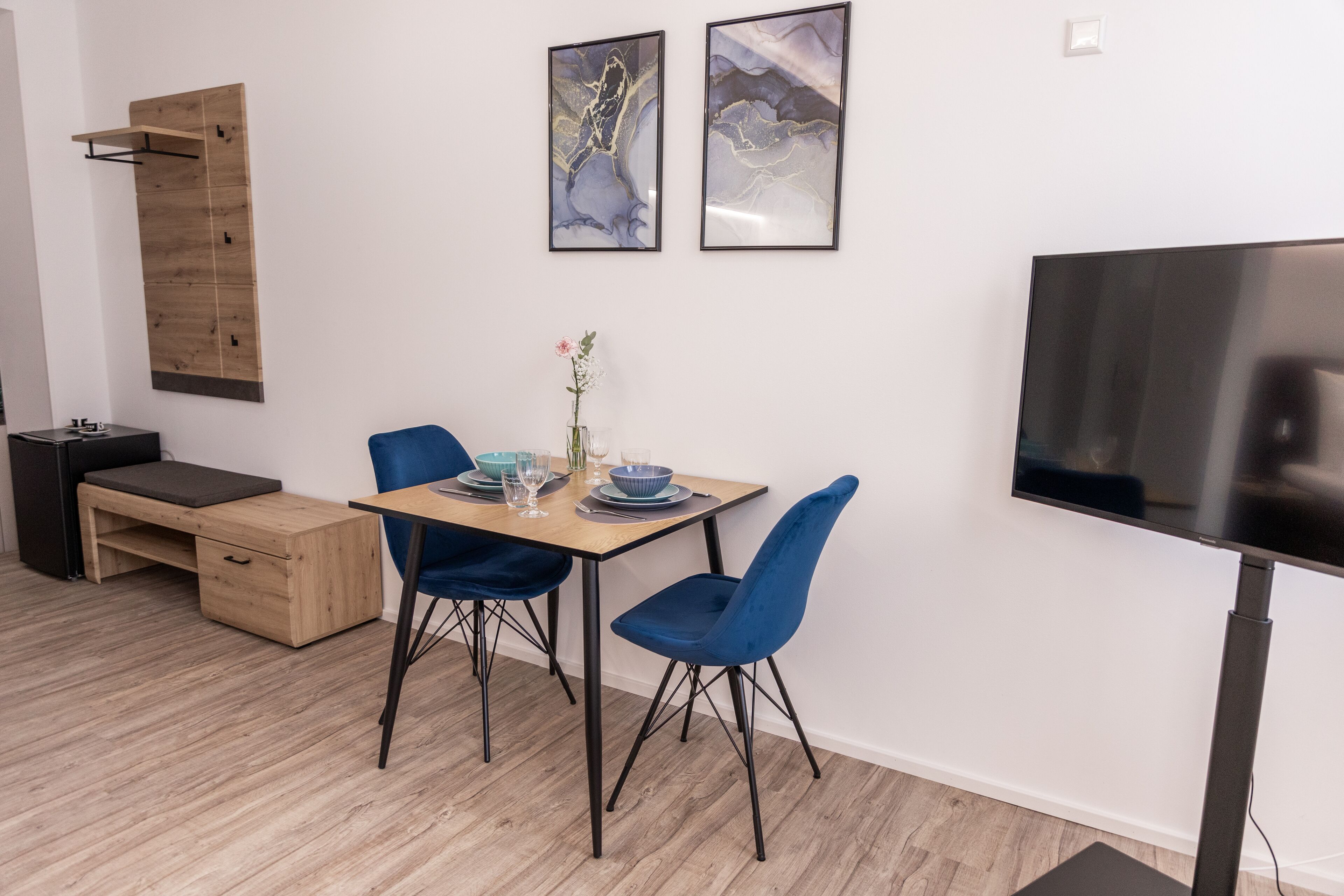 A modern dining area with a wooden table, blue chairs, and a flat-screen TV mounted on the wall.