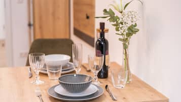A wooden dining table set with plates, bowls, glasses, cutlery, a bottle, and a vase with flowers.