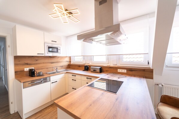 A modern kitchen with white cabinets, a wooden countertop, a built-in microwave, and a coffee maker. - Apartments am Marktplatz (Bad Urach)