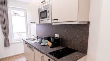A compact kitchen with a microwave, stove, and coffee maker. It features light-colored cabinets and a granite countertop.