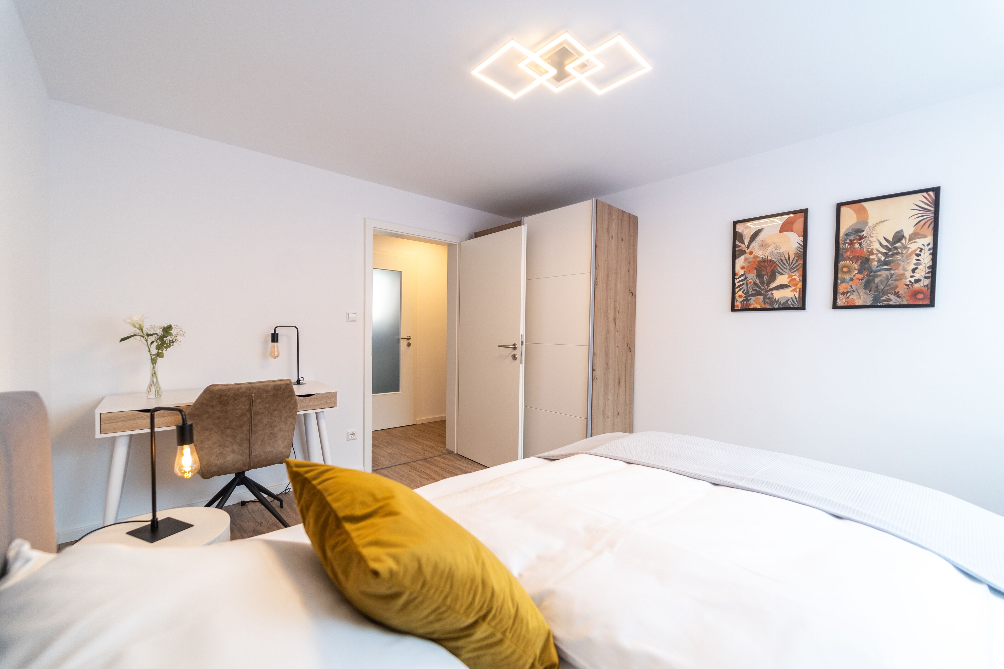 Une chambre d’hôtel moderne équipée d’un lit, d’un bureau, d’une chaise et d’une porte donnant sur une autre pièce.