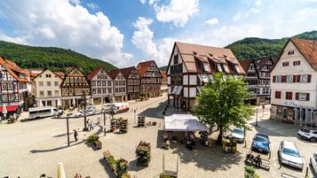 A traditional European town square with cobblestone pavement, historic half-timbered buildings, and a central open space with a white tent.