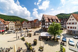Ein traditioneller europäischer Stadtplatz mit Kopfsteinpflaster, historischen Fachwerkhäusern und einem zentralen Platz mit einem weißen Zelt.