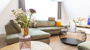 A modern living room with a sectional sofa, a round coffee table, and a vase with flowers. - Apartments am Marktplatz (Bad Urach)
