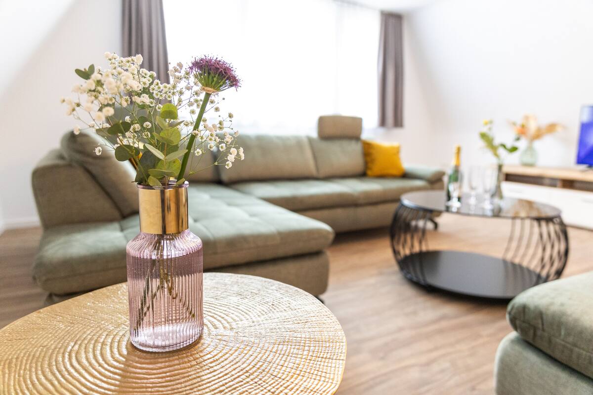 A modern living room with a sectional sofa, a round coffee table, and a vase with flowers.
