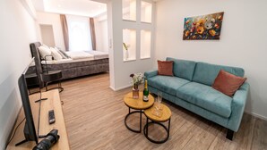 A modern living room with a sofa, a coffee table, a TV, and a bed in the background. - Apartments am Marktplatz (Bad Urach)