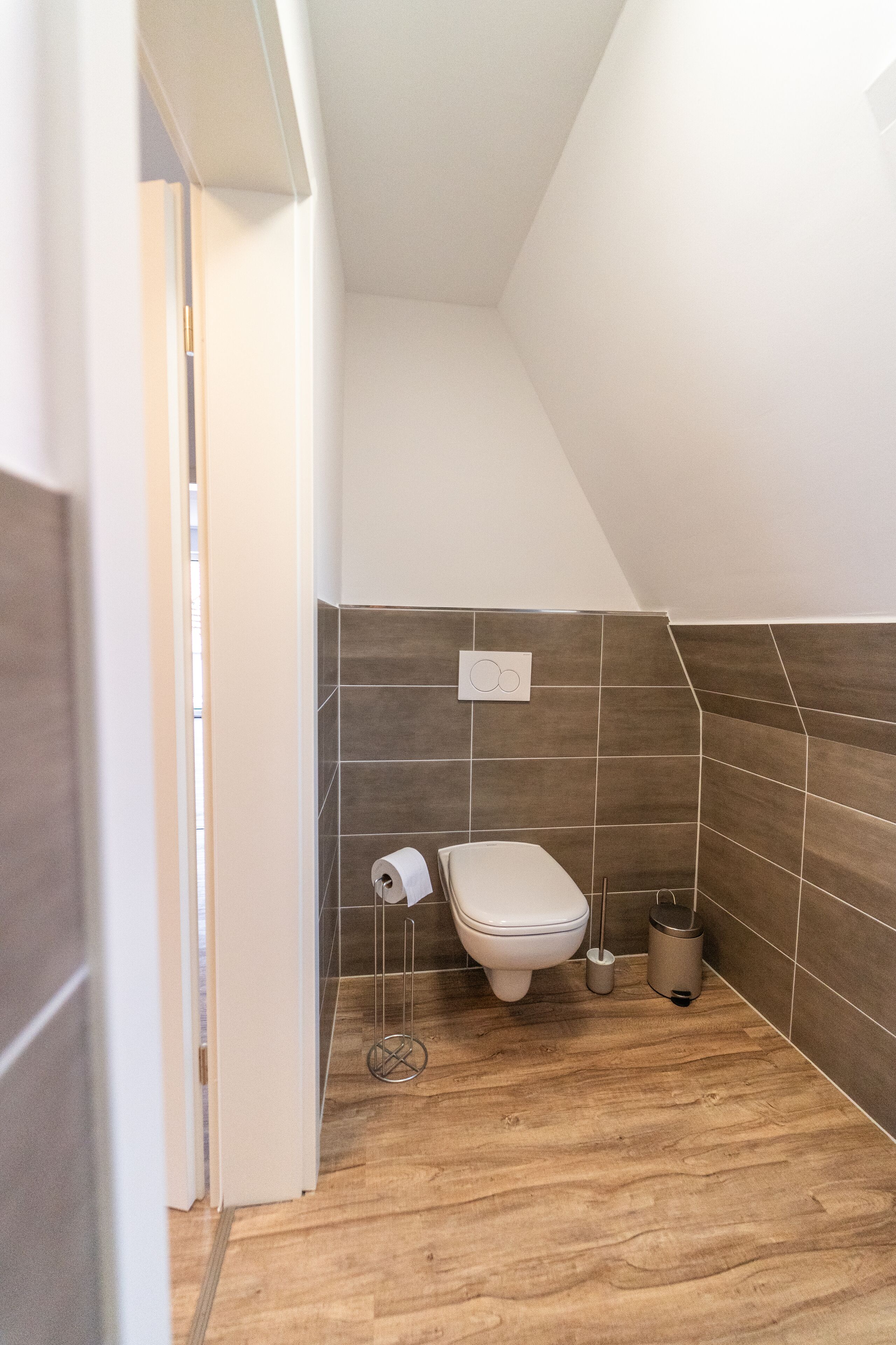 A small, modern bathroom with a toilet, a roll of toilet paper, and a trash can.