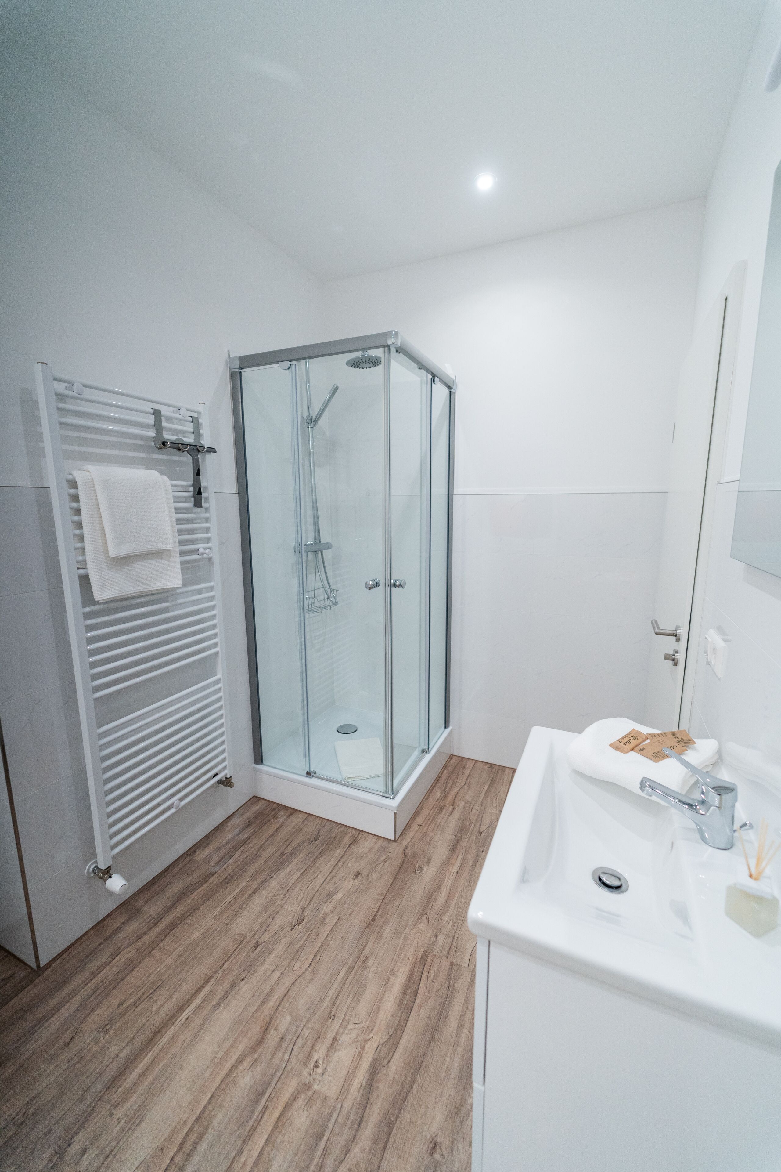 A modern bathroom with a glass shower enclosure, a white sink, and a towel rack.