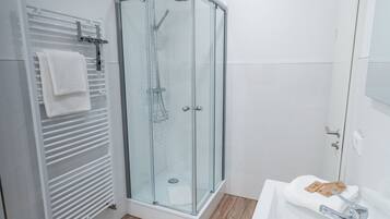 A modern bathroom with a glass shower enclosure, a white sink, and a towel rack.
